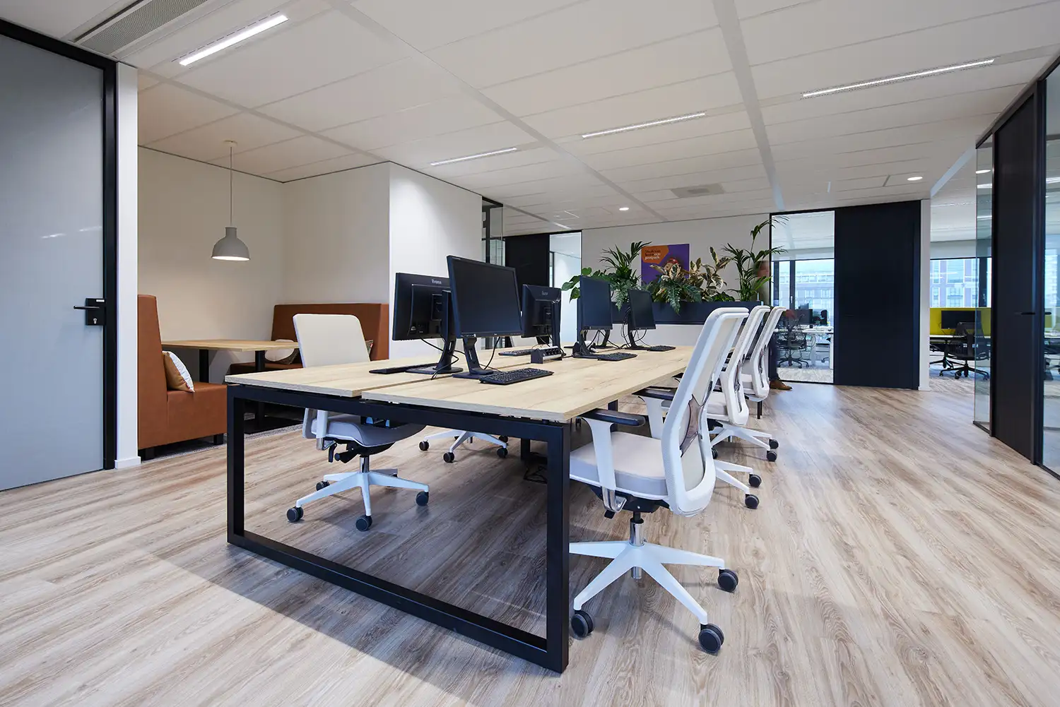 Ruimte voor studie en werken met grote tafel met houten blad en computers waaraan royale witte bureaustoelen staan.