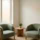 Moderne wachtkamer met twee saliegroen gestoffeerde stoelen, een houten bijzettafel met kamerplant en zacht natuurlijk licht.