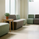 Moderne wachtkamer in een zorginstelling met saliegroen gestoffeerde stoelen, een lichte eiken bijzettafel met plant en zacht daglicht.