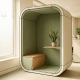 Akoestische privacypod met salie groene bekleding, houten plank met plant en Scandinavisch design in licht Nederlands kantoor.