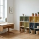 Ergonomisch kinderbureau van warm eikenhout bij raam met natuurlijk daglicht, modulaire boekenkast met kunstbenodigdheden en plantjes.