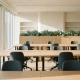 Moderne open kantoorruimte met verstelbare eiken bureaus, ergonomische stoelen en grote ramen die zacht ochtendlicht binnenlaten.