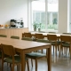 Moderne bedrijfskantine met houten tafels, stapelstoelen en een zelfbedieningsbalie met koffiemachine, verlicht door groot daglicht.