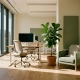 Lege moderne open kantoorruimte met ergonomisch zit-sta bureau, loungebank en grote ramen met warm natuurlijk licht.